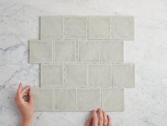 two hands on a white marble tile with one hand reaching for the tiles to be laid out