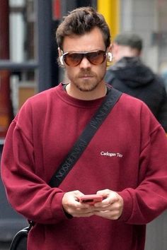 a man in a red sweatshirt is looking at his cell phone while walking down the street