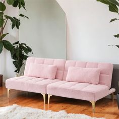 a pink couch sitting on top of a hard wood floor next to a mirror and potted plant