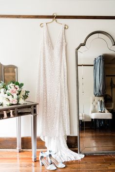 a wedding dress hanging on a rack in front of a mirror and flower bouquets