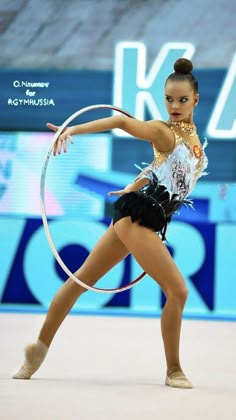 a woman is performing with a hoop in her hand and wearing a white shirt, black shorts and gold necklace