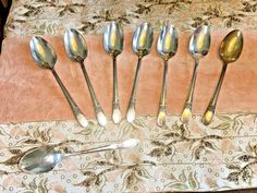 six silver spoons are lined up on a table with a pink and white cloth