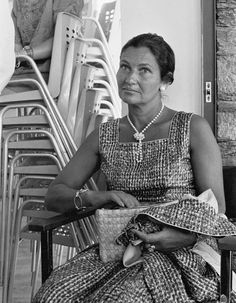 an old photo of a woman sitting in a chair next to stack of chairs and looking off into the distance