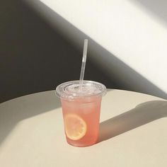 a plastic cup with a straw and an orange slice on the rim sitting on a table