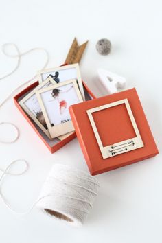 an orange box with some pictures in it on top of a white table next to scissors and thread