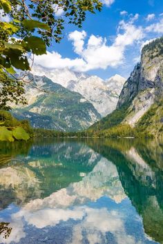 a mountain lake surrounded by trees and mountains in the distance with clouds reflected on it