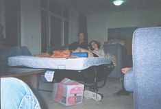 three people are sitting on a bed in a room with blue couches and other furniture