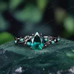 a ring with green stones and leaves on it, sitting on top of a rock