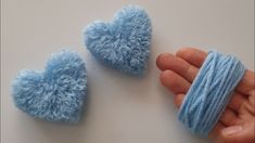 two small blue hearts are being held up by someone's hand and yarn is wrapped around them