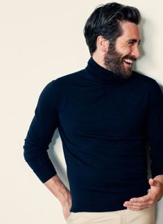 a man with his hands on his hips wearing a black turtle neck sweater and khaki pants