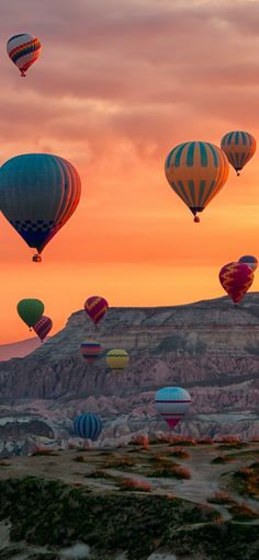 many hot air balloons are flying in the sky at sunset or dawn over mountains and valleys