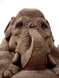 an elephant sand sculpture sitting on top of a sandy beach with its trunk curled up