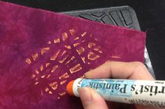 a hand holding a tube of glue next to a purple book with writing on it