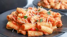 pasta with tomato sauce and parmesan cheese on black plate next to silverware