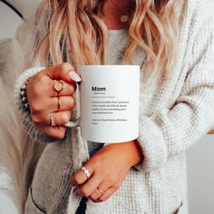 a woman holding a white coffee mug in her right hand with the words mom on it