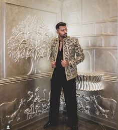 a man standing in front of a silver wall with an intricate design on it's side