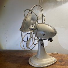 an old style fan sitting on top of a wooden table next to a wall mounted light