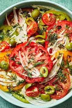 a large bowl filled with lots of different types of tomatoes and other vegetables on top of a blue surface