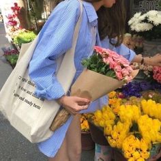 a woman is holding flowers in her hands while walking down the street with a bag