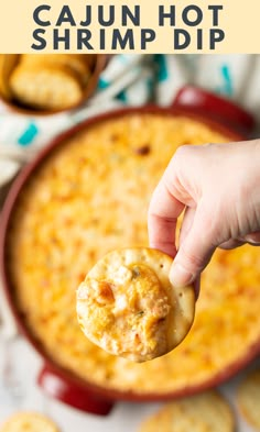 a hand holding a cracker over a bowl of cheesy cajun hot shrimp dip