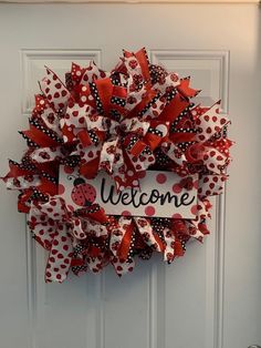 a red and white wreath with ladybug on it that says welcome hanging on the front door