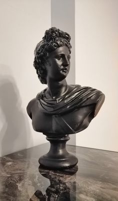 a black busturine sitting on top of a marble table next to a white wall