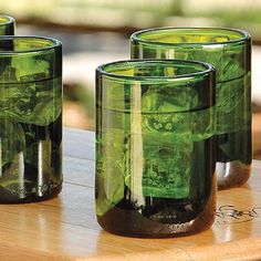 three green glass cups sitting on top of a wooden table next to eachother