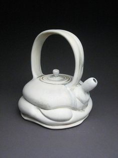 a white ceramic teapot with an animal design on the front and side, sitting on a black surface