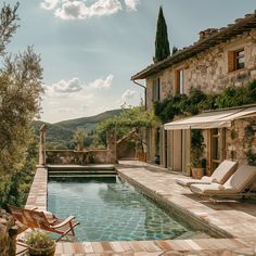 an outdoor swimming pool with chaise lounges next to it and a stone house in the background