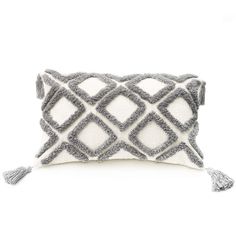 a gray and white pillow with tassels on the front, sitting on a white surface