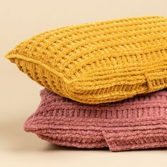 three knitted pillows stacked on top of each other in pink, yellow and purple