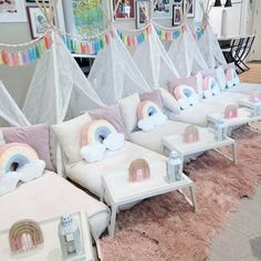 a room filled with lots of white couches covered in pillows and rainbows hanging from the ceiling