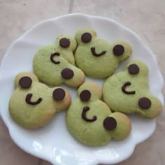 green cookies with chocolate eyes and noses on a white plate sitting on a tile floor