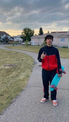 a young man holding a skateboard while standing on a sidewalk in front of houses