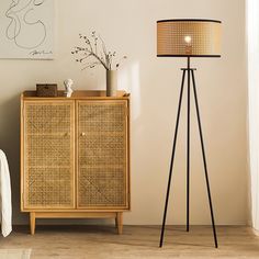 a floor lamp next to a wicker cabinet with a vase on top and a painting above it