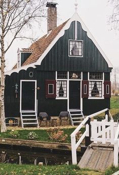 a black house with red shutters next to a tree and grass covered lawn area