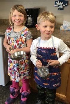 two young children standing next to each other holding pots and pans