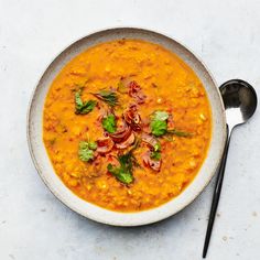 a white bowl filled with carrot soup and garnished with cilantro leaves