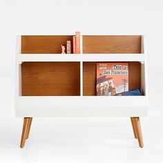 a white book shelf with books on top and two wooden legs, in front of a white background