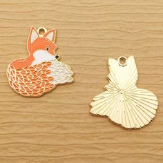 two charms that are sitting on top of a wooden surface, one has a fox and the other has a fish