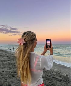 a woman taking a photo with her cell phone on the beach at sunset or dawn