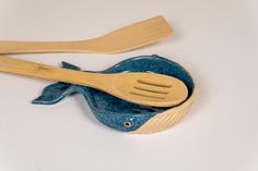 two wooden utensils are sitting in a blue whale shaped bowl with spoons