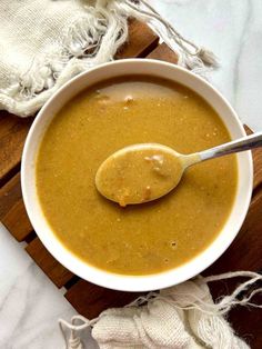 a white bowl filled with soup on top of a wooden table next to a spoon