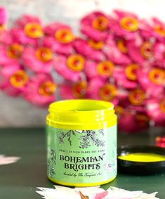 a yellow jar sitting on top of a table next to pink flowers