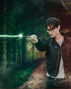 a young man holding a green light wand in his hand while standing on a forest path