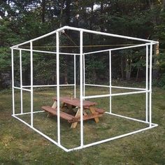 a white metal structure with picnic table in the grass