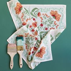 a brush and two napkins sitting on top of a green tablecloth with orange flowers