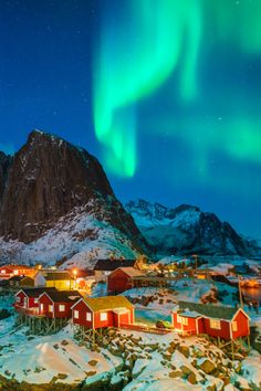 the northern lights shine brightly over small houses and snow - capped mountains in norway's lofoss valley