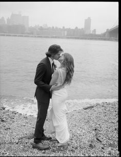 a man and woman kissing on the beach by the water in front of a cityscape