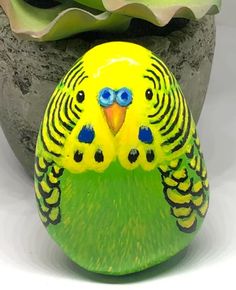 a yellow and green bird painted on top of a rock next to a potted plant